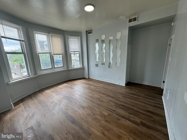 unfurnished room featuring dark wood-style floors, visible vents, and baseboards