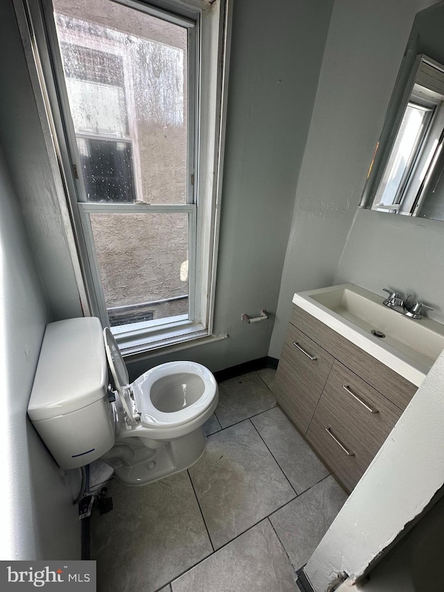 half bathroom with baseboards, vanity, toilet, and tile patterned floors