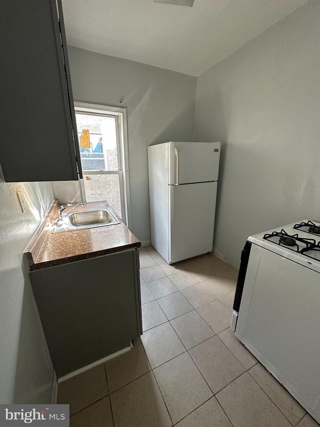 kitchen with light tile patterned flooring, range with gas stovetop, a sink, and freestanding refrigerator