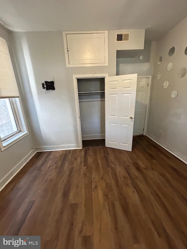 unfurnished bedroom featuring dark wood-style flooring, a closet, visible vents, and baseboards