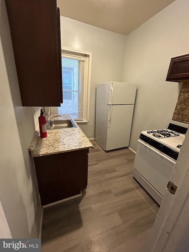 kitchen featuring white appliances, a sink, light countertops, dark brown cabinets, and light wood finished floors