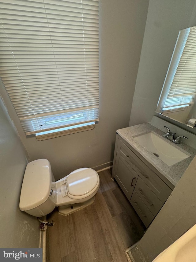 half bathroom featuring vanity, wood finished floors, toilet, and baseboards