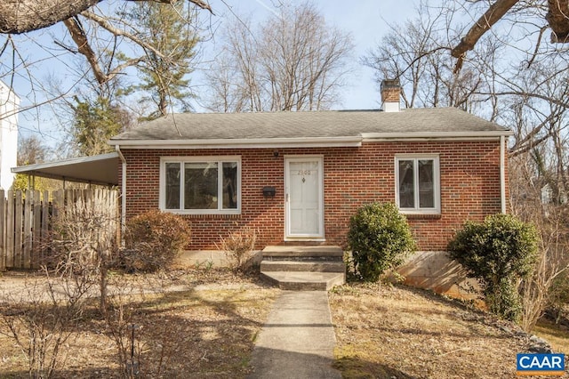 view of front of home featuring brick siding, a chimney, fence, and an attached carport