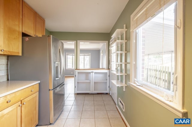 kitchen featuring light tile patterned floors, baseboards, decorative backsplash, stainless steel fridge with ice dispenser, and light countertops