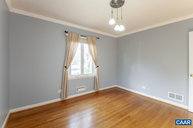 spare room with ornamental molding, wood finished floors, visible vents, and baseboards