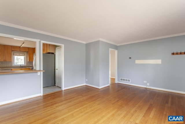 unfurnished living room with visible vents, baseboards, light wood-style flooring, ornamental molding, and a sink