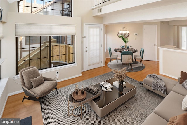 living room with visible vents, a towering ceiling, an inviting chandelier, and wood finished floors