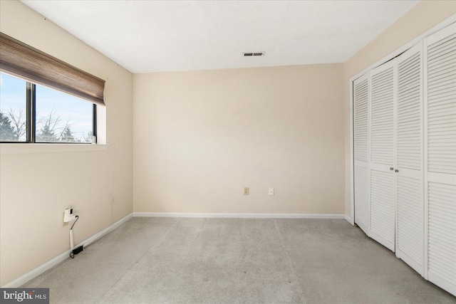 unfurnished bedroom featuring a closet, light colored carpet, visible vents, and baseboards