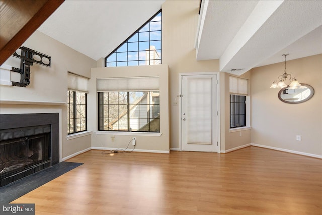 unfurnished living room featuring a fireplace with flush hearth, a chandelier, baseboards, and wood finished floors