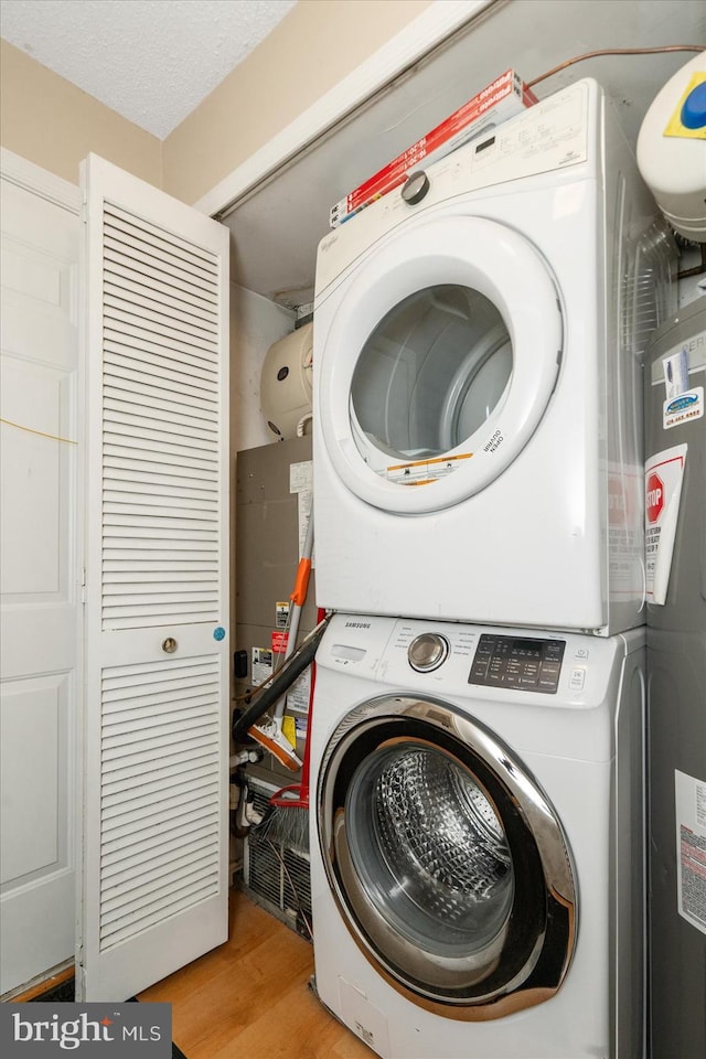 clothes washing area featuring laundry area, stacked washer and clothes dryer, a textured ceiling, and wood finished floors