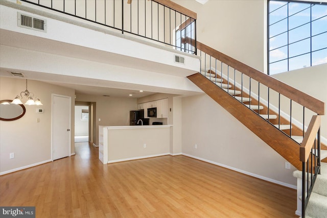 unfurnished living room featuring stairway, a high ceiling, visible vents, and a chandelier