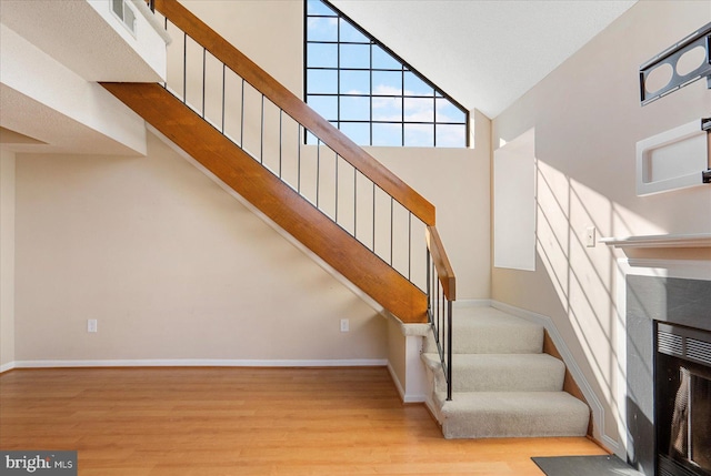 stairway featuring a premium fireplace, wood finished floors, visible vents, a towering ceiling, and baseboards