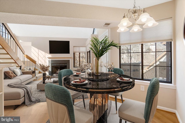 dining room with baseboards, visible vents, wood finished floors, an inviting chandelier, and a fireplace