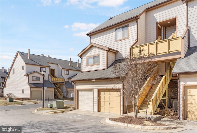 multi unit property featuring a garage, a shingled roof, and stairway