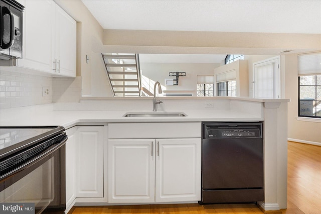 kitchen with a peninsula, a sink, black appliances, white cabinetry, and backsplash