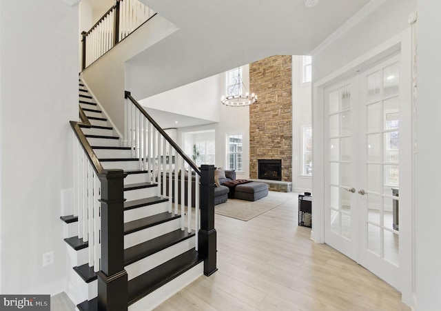 foyer with french doors, stairway, a high ceiling, a stone fireplace, and light wood-style floors