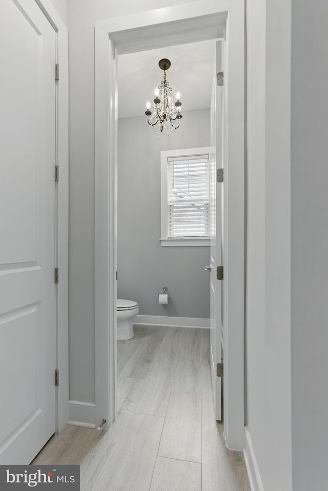 bathroom with toilet, baseboards, a chandelier, and wood finished floors