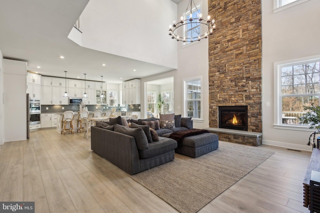 living room with a stone fireplace, light wood-style flooring, visible vents, baseboards, and an inviting chandelier