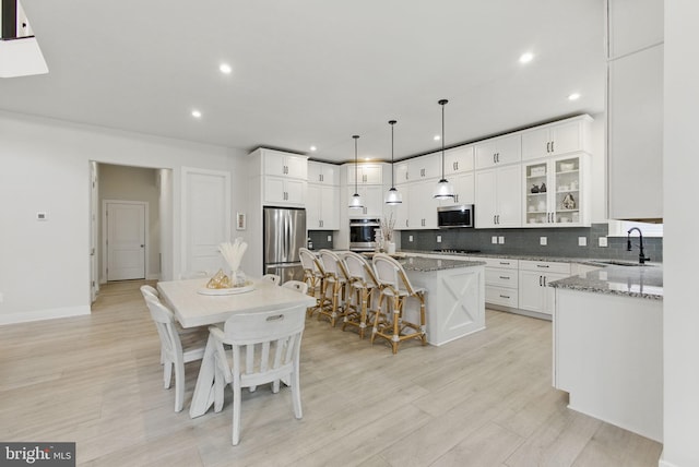 kitchen featuring a center island with sink, decorative backsplash, appliances with stainless steel finishes, light stone countertops, and a kitchen bar