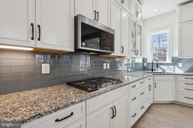 kitchen featuring light stone counters, white cabinetry, stainless steel appliances, and a sink