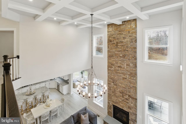 living area featuring a fireplace, coffered ceiling, light wood-type flooring, beamed ceiling, and an inviting chandelier