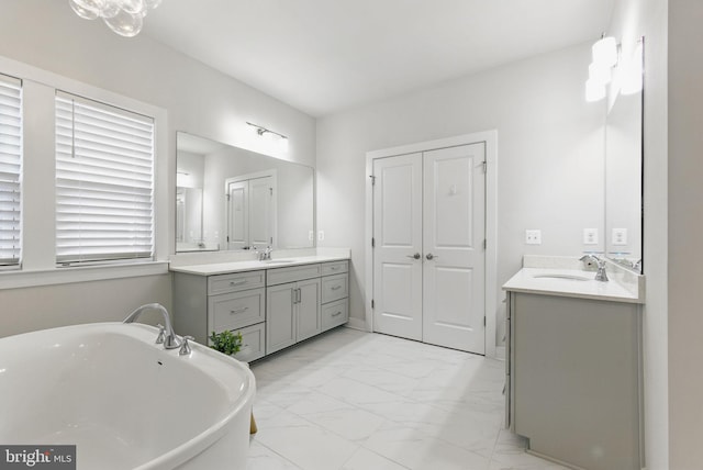 full bathroom with marble finish floor, a freestanding bath, two vanities, and a sink