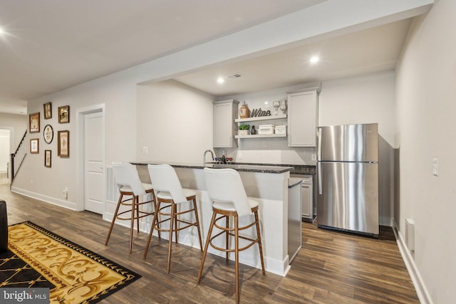 kitchen with open shelves, dark wood finished floors, a kitchen bar, and freestanding refrigerator