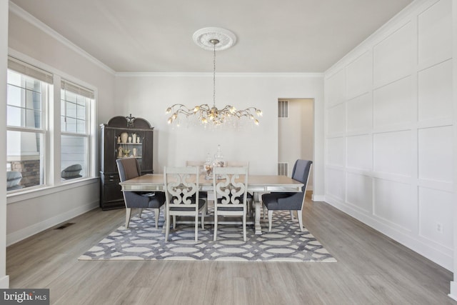 dining space with visible vents, ornamental molding, a decorative wall, and wood finished floors