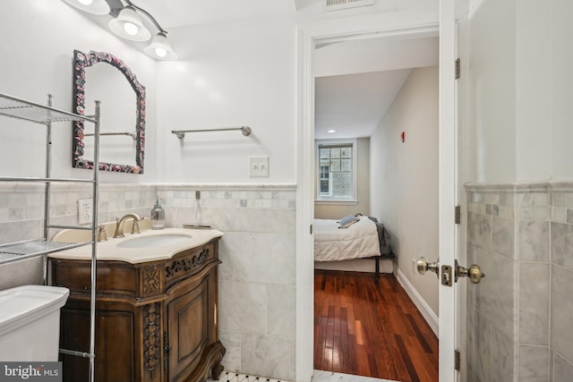 bathroom with connected bathroom, toilet, wood finished floors, vanity, and tile walls