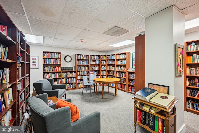 living area featuring wall of books, carpet, and a drop ceiling