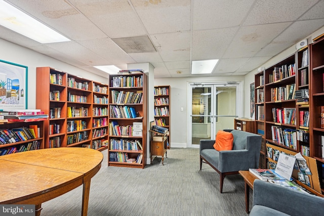 living area featuring wall of books, baseboards, carpet floors, and a paneled ceiling