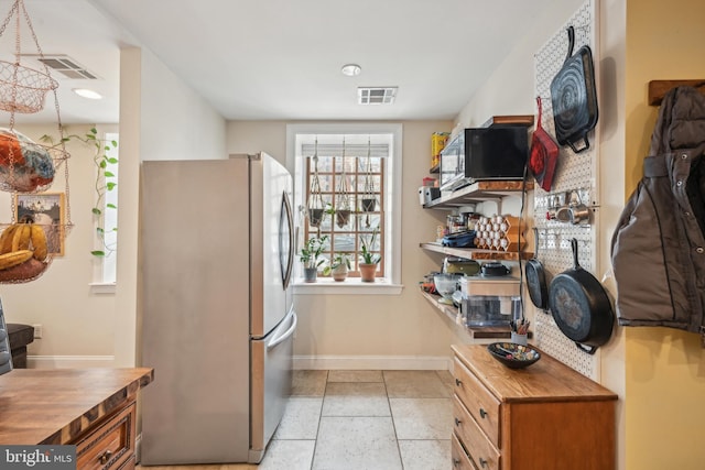 kitchen with black microwave, butcher block counters, visible vents, and freestanding refrigerator