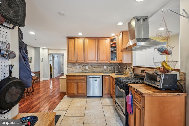 kitchen featuring extractor fan, stainless steel appliances, decorative backsplash, brown cabinetry, and glass insert cabinets