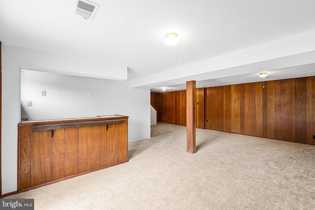 finished below grade area featuring wooden walls, visible vents, and light carpet