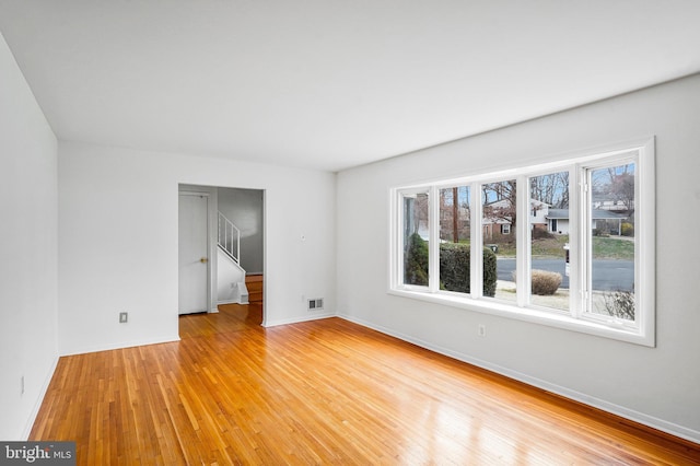 empty room featuring stairway, light wood-style floors, visible vents, and baseboards