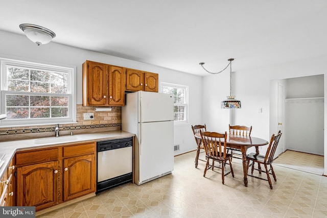 kitchen featuring brown cabinetry, white appliances, light countertops, and a sink