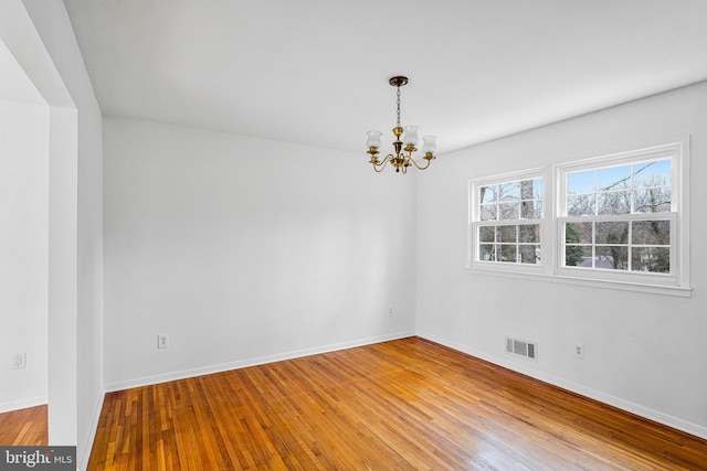 spare room with hardwood / wood-style flooring, visible vents, baseboards, and a chandelier