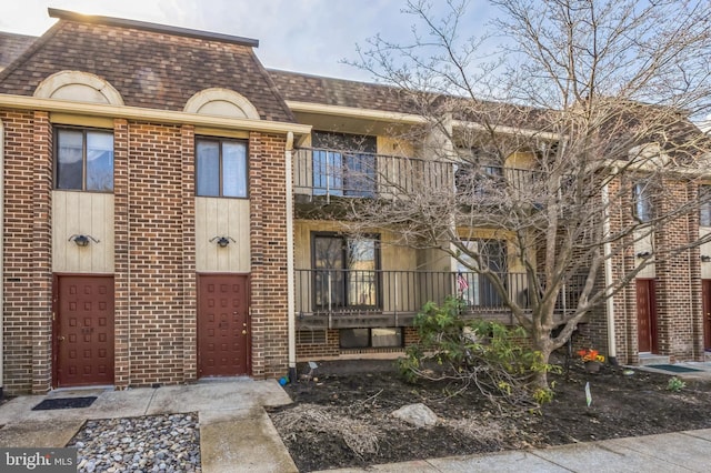 exterior space featuring mansard roof, roof with shingles, a balcony, and brick siding