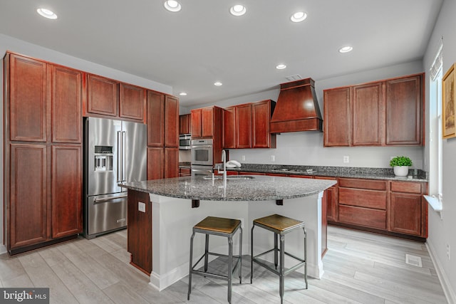 kitchen with a breakfast bar, custom exhaust hood, stainless steel appliances, light wood-style flooring, and a sink