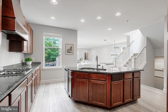 kitchen with dark stone countertops, stainless steel gas stovetop, light wood-style flooring, and a sink