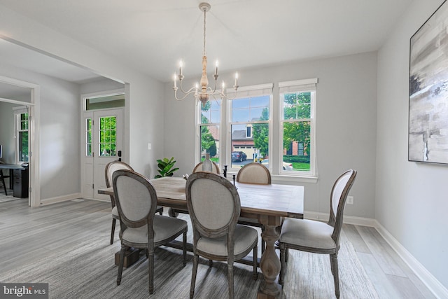 dining area with light wood-type flooring, a wealth of natural light, baseboards, and an inviting chandelier