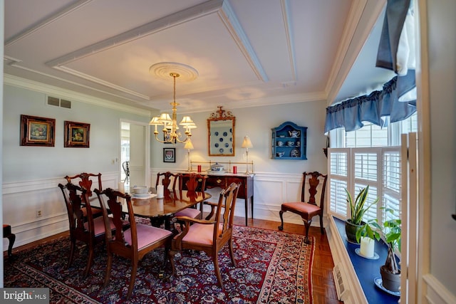 dining area with an inviting chandelier, wainscoting, visible vents, and crown molding