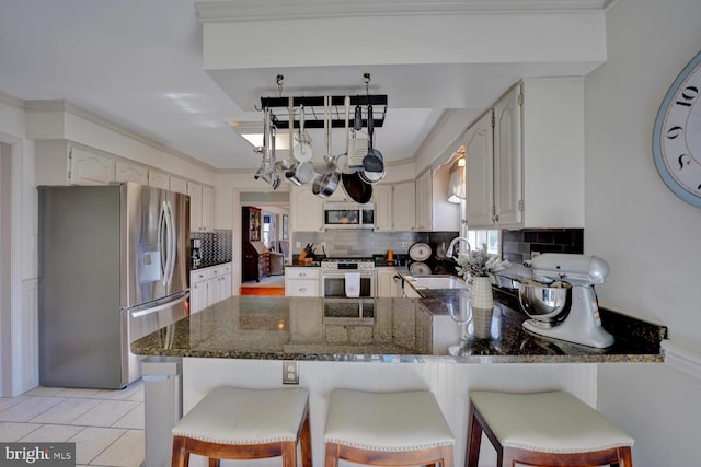 kitchen with light tile patterned floors, stainless steel appliances, a peninsula, a sink, and decorative backsplash