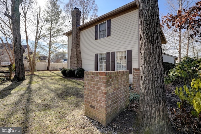 view of side of home featuring a yard, a chimney, and fence