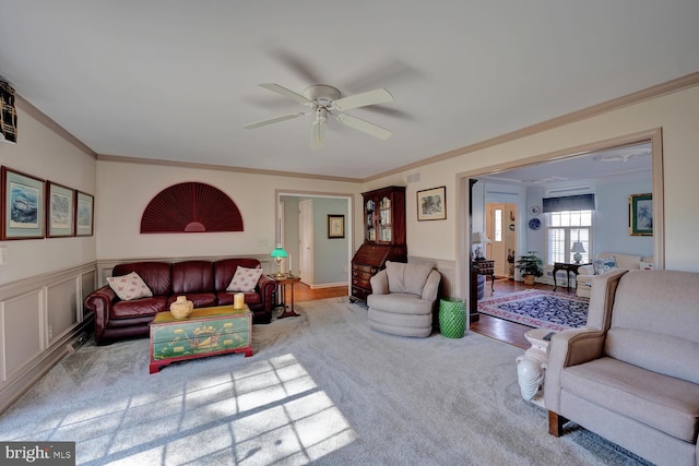 living area featuring a decorative wall, wainscoting, a ceiling fan, and crown molding