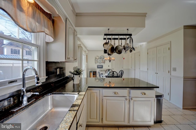 kitchen with a peninsula, dark stone countertops, ornamental molding, and a sink