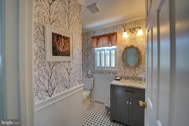 bathroom featuring toilet, a wainscoted wall, visible vents, ornamental molding, and wallpapered walls