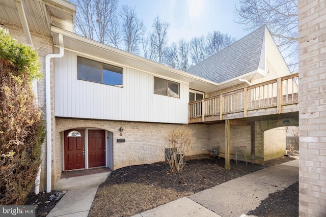 rear view of house featuring a shingled roof and brick siding