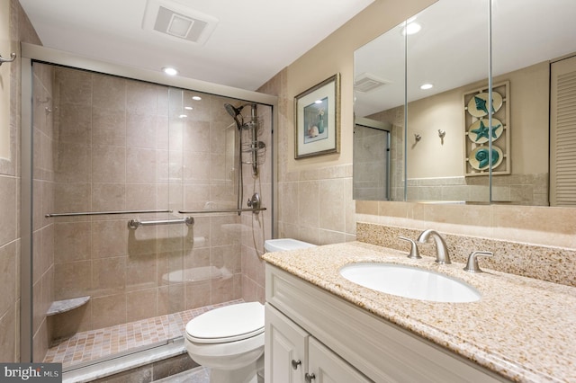 bathroom with toilet, a shower stall, visible vents, and tile walls