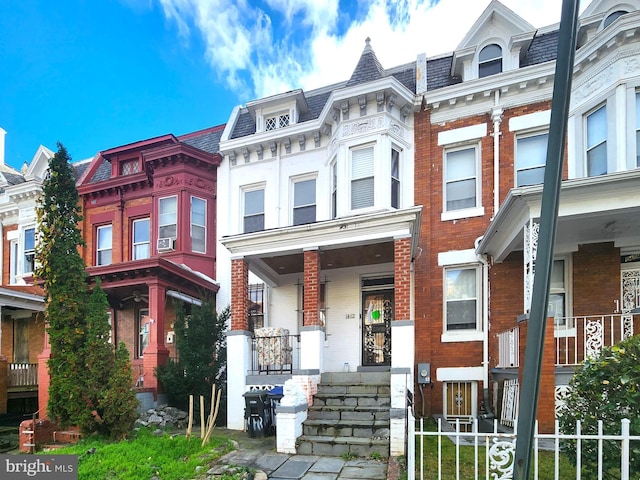 view of front of property featuring a high end roof, covered porch, brick siding, and mansard roof